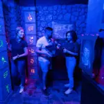 Friends collaborating in a neon-lit mystery room at Escapology escape rooms.